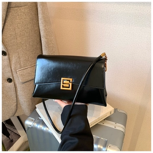 Detail of a black leather envelope bag with gold hardware on a suitcase and book