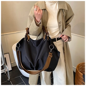 Detail of black nylon tote bag featuring brown fabric straps and silver metal hardware