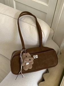 Bolso de hombro de ante marrón con colgante de perrito sobre sofá beige
