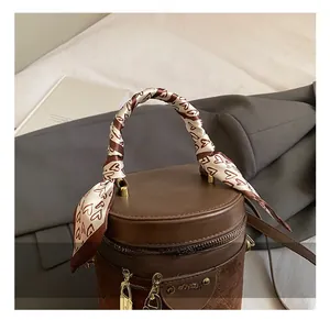Detail of a brown cylindrical bucket bag with leather texture and heart silk scarf handle