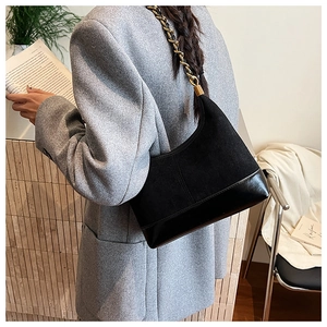 Detail of a black hobo shoulder bag with matte texture and gold chain strap on a model