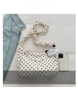Detailed close-up of a white polka dot tote bag with pleated straps and cute plush pendant