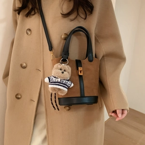 Détail du sac seau en daim marron avec poignée en cuir et charmant petit ours en peluche