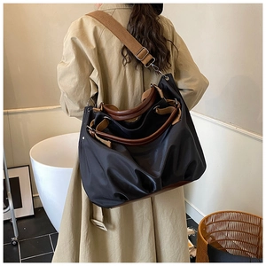 Detail view of a large black nylon tote bag featuring brown leather handles and pleated fabric