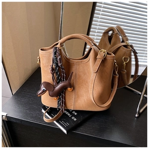 Brown matte leather bucket bag with dog pendant and contrast stitching on dark wood surface