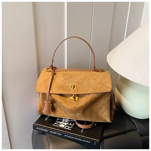 Detail of a brown suede tote bag with a gold metal clasp placed on art books