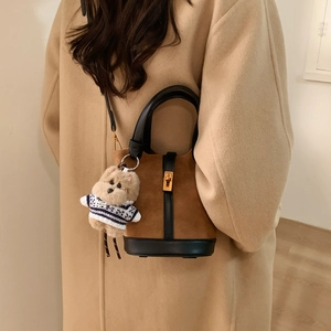 Gros plan du sac seau montrant le daim marron, les bordures en cuir et le charm ours