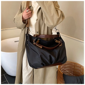 Detail view of large black canvas tote bag with brown leather handles worn over a trench coat