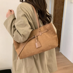 Detail of a brown matte leather tote bag with elegant side straps and decorative pendant