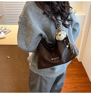 Detail of vintage brown leather bag with plush bear charm and metallic brand tag