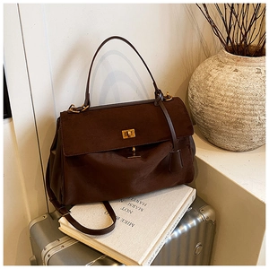 Detail of dark brown suede handbag with golden twist lock and leather trim on a suitcase