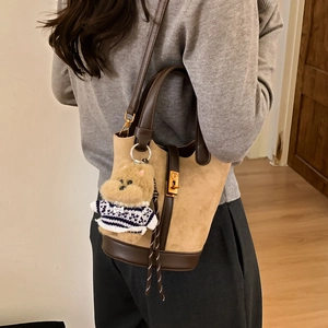 Détail du sac seau en daim avec bordure en cuir marron et breloque chien en peluche