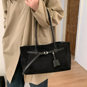 Detail of black suede tote bag with silver buckle and leather tag on a stylish model