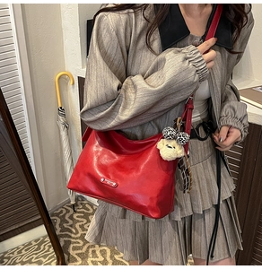 Macro view of a red Hobo bag featuring a silver metal plate and cute teddy bear charm