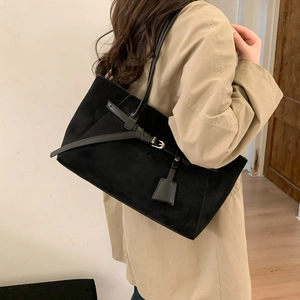 Close-up of a matte black suede tote bag with leather strap detail on a model's shoulder