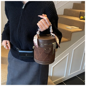 Detail of a brown cylindrical bucket bag with quilted stitching and a decorative heart scarf