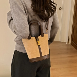 Vue latérale du sac seau bicolore en daim beige et cuir marron porté par un mannequin