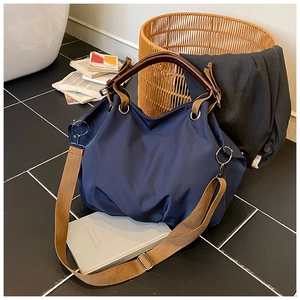 Detail of navy blue nylon tote bag with brown handles and khaki adjustable shoulder strap