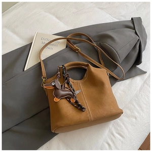 Detail of camel suede bucket bag with contrast stitching and dachshund charm accessory