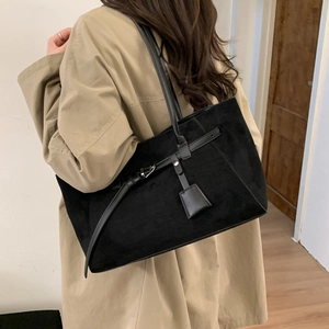 Detail of black suede tote bag featuring metallic buckle and long leather pendant tag