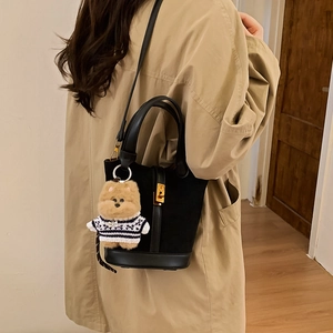 Détail d'un sac seau noir avec pendentif chien porté sur un trench-coat beige élégant