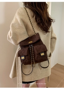 Close-up of quilted dark brown suede backpack with gold chain straps on a model