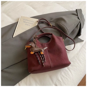 Detail of burgundy frosted leather bucket bag with white stitching and dog charm