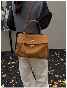 Brown vintage suede tote bag with golden twist lock detail and autumn leaf background