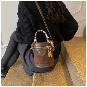 Detail of a brown bucket bag with quilted suede, leather finish, and scarf-wrapped handle