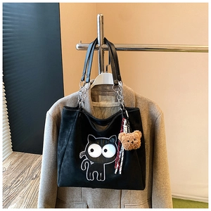 Détail du sac cabas en daim noir avec patch chat et breloque ours sur un portemanteau