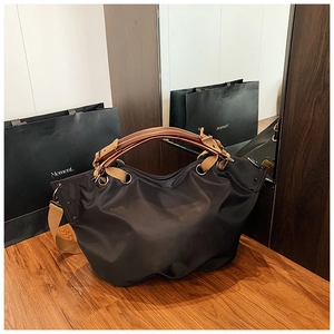 Detail of black nylon tote bag with brown resin handles and wide canvas shoulder strap