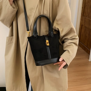 Détail d'un sac seau noir en daim avec boucle dorée et anses en cuir sur un trench-coat