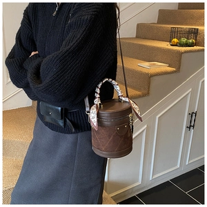 Detail of dark brown cylindrical bucket bag with quilted stitching and silk scarf handle