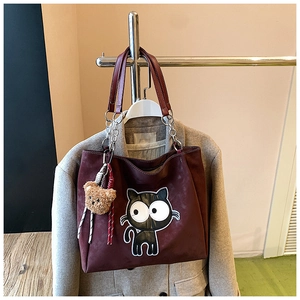 Détail du cabas en daim bordeaux avec écusson chat et breloque ours sur un manteau