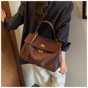 Macro detail of brown suede tote bag featuring dual golden twist locks and handle