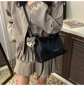 Detail of black leather shoulder bag with bear pendant worn by model in warm room