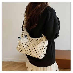 Detail of beige polka dot tote bag featuring ruffled shoulder strap and plush dog charm