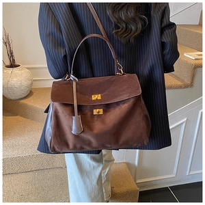 Brown suede tote bag with golden twist locks shown on stairs in a minimal scene
