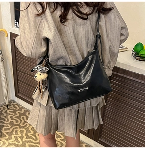Detail view of black PU leather shoulder bag featuring a cute plush bear charm with bow tie