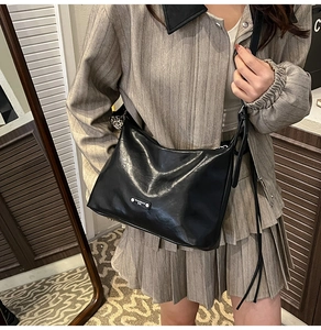 Detail of minimalist black leather tote bag with silver logo plate and tassel strap