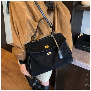Detail view of large black suede tote bag with golden twist lock and adjustable strap