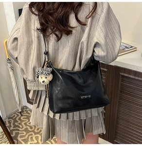 Detail of black matte shoulder bag featuring a cute plush dog charm with leopard bow