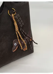 Close-up of a brown leather tote bag featuring a cute dachshund dog charm and woven strap