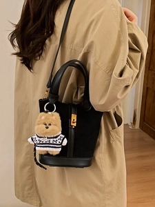 Sac seau noir mat avec fermoir doré et charm chien porté par un mannequin de mode