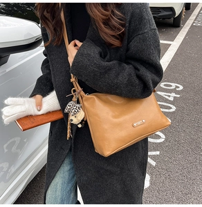Brown faux leather crossbody bag with a leopard bear charm shown in a street style view