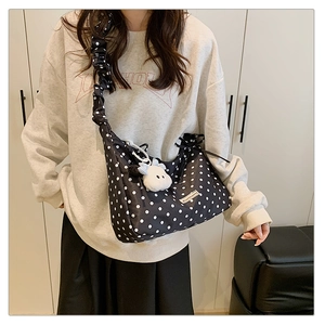 Detail of black polka dot dumpling bag with ruched strap and white sheep plush keychain