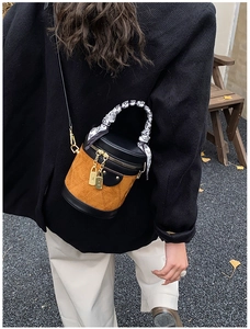 Detail of a brown suede cylinder bag with heart scarf handle and gold locks worn by model