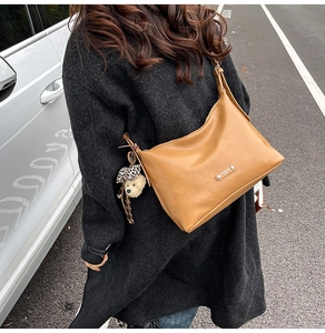 Detail of a brown leather crescent shoulder bag featuring a cute plush bear charm