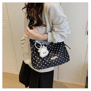 Close-up of black polka dot pleated crossbody bag with a cute white plush charm