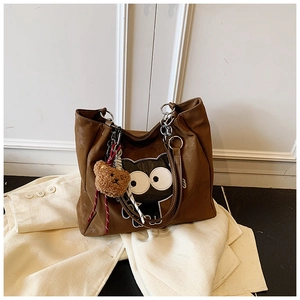 Détail d'un sac cabas marron avec motif chat et bandoulière chaîne sur un blazer blanc